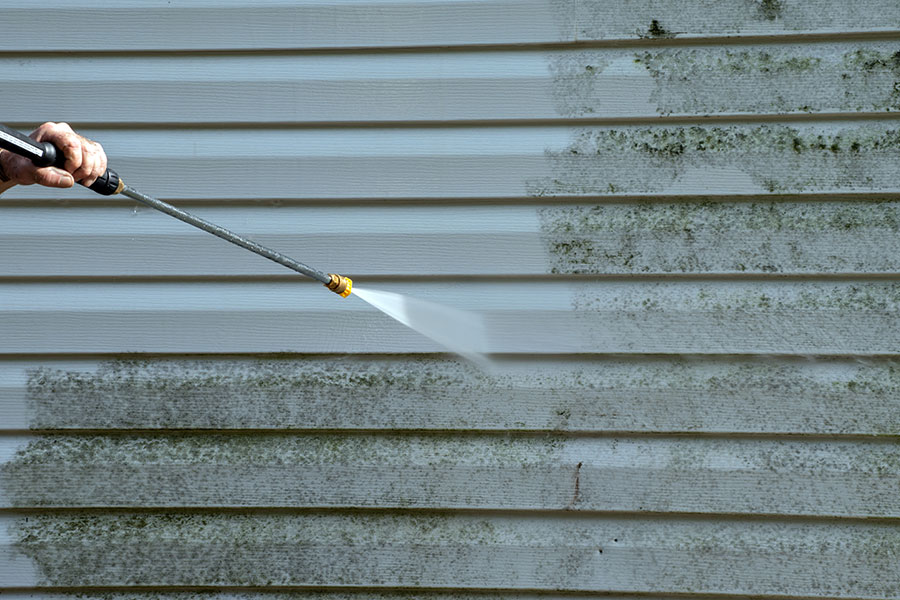 A professional power washing expert using a power washer to clean the dirt and algae off of the vinyl siding of a home in Kansas City, MO.