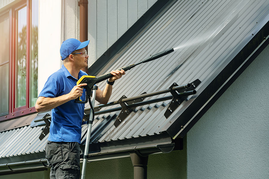A professional technician power washes the roof of a residence in Kansas City, MO while adhering to the appropriate safety measures to keep himself from harm and protect the property from damages.