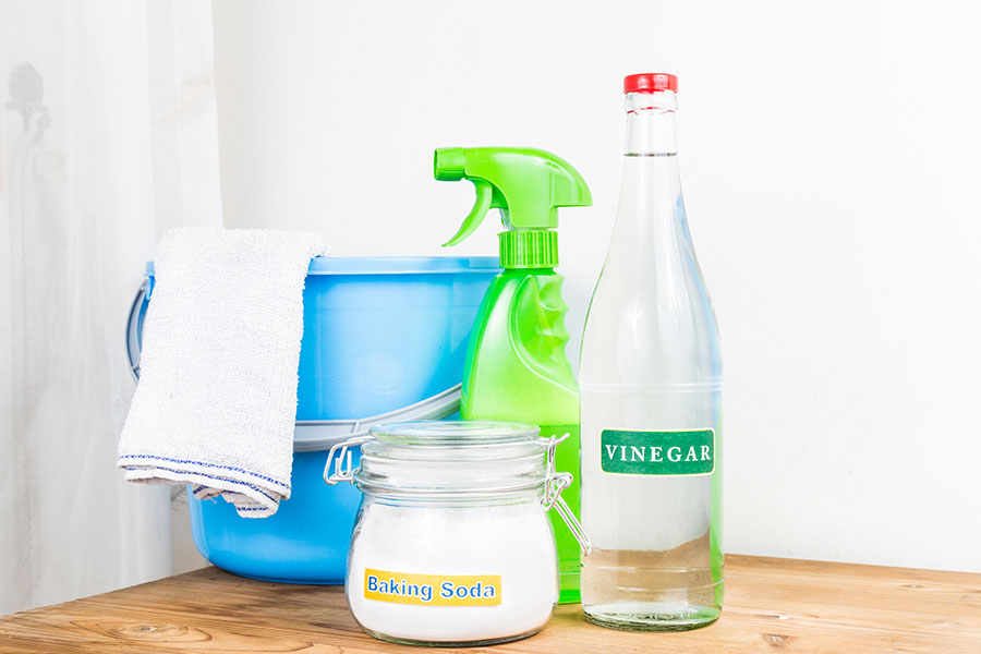 A variety of cleaning substances sits on a table inside a Kansas City, MO home, including a bucket, a spray bottle of water, baking soda, and vinegar. All these things can be used to help get our grease stains at your Kansas City, MO home.