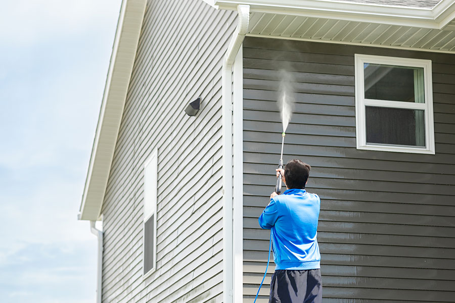 A power washing expert using commercial power washing equipment to clean the siding of a home in Kansas City, MO.
