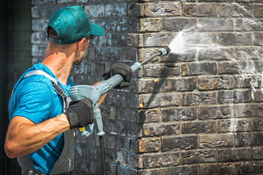 A power washing professional in a blue shirt using commercial power washing equipment on a brick home in Kansas City, MO.