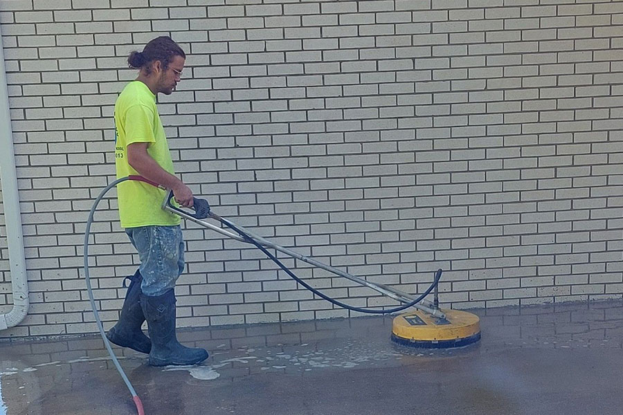 A power washing technician in Kansas City, MO using commercial equipment to power wash a concrete driveway for a residential home.